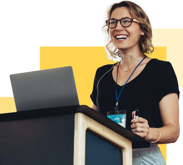 photo of a smiling woman standing at a podium with a laptop on it
