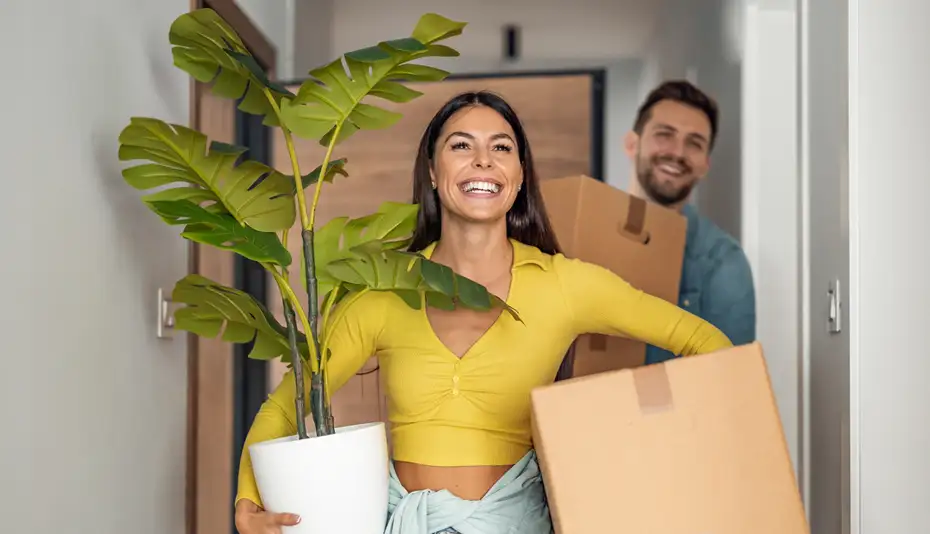 photo of a smiling couple carrying moving boxes
