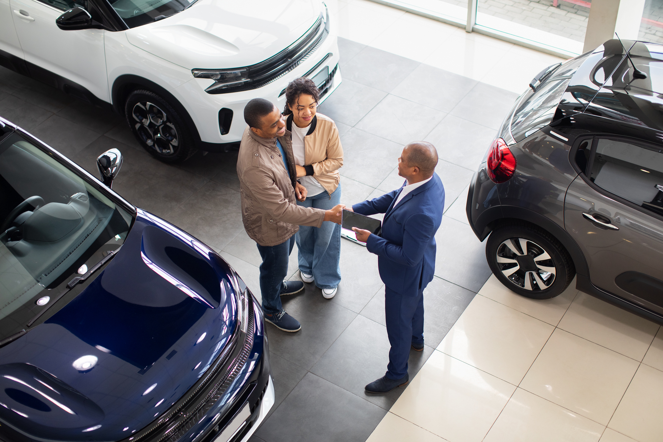 African American couple shaking hands with dealer in showroom, celebrating car purchase automotive